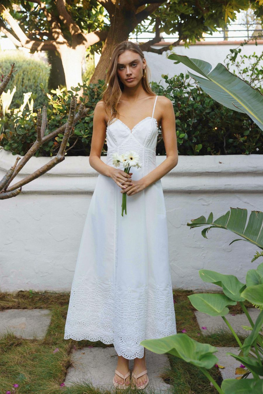 Woman in a white dress holding flowers in a garden setting