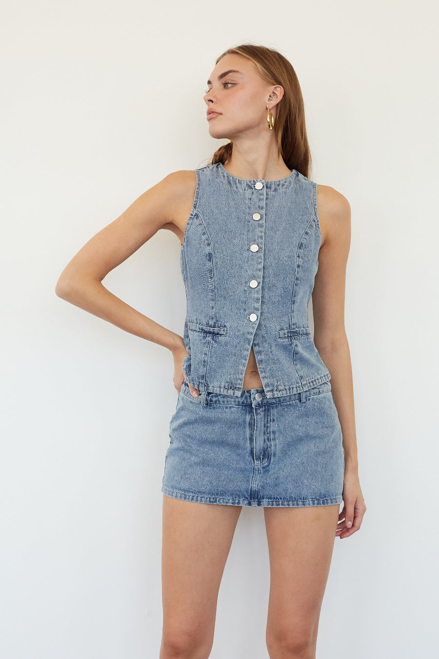A woman modeling a light blue denim sleeveless top and matching denim mini skirt against a plain white background.