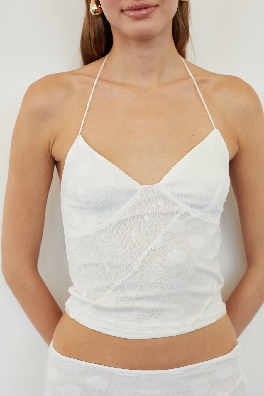 A close-up of a model wearing a white halter crop top with a textured, dotted fabric pattern and a wrap-style front.