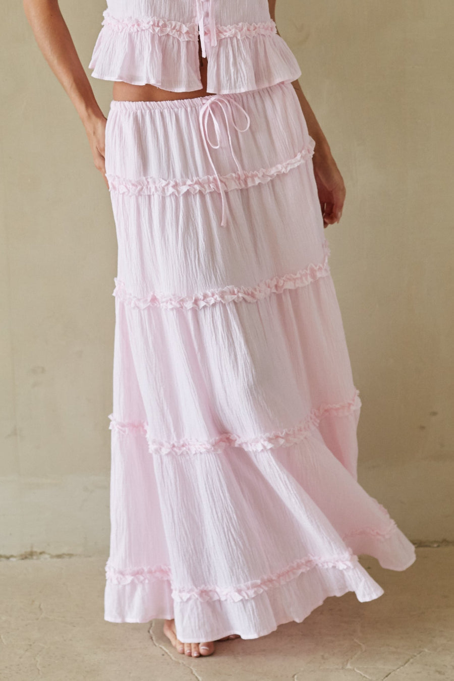 Woman wearing a pink tiered dress against a beige background