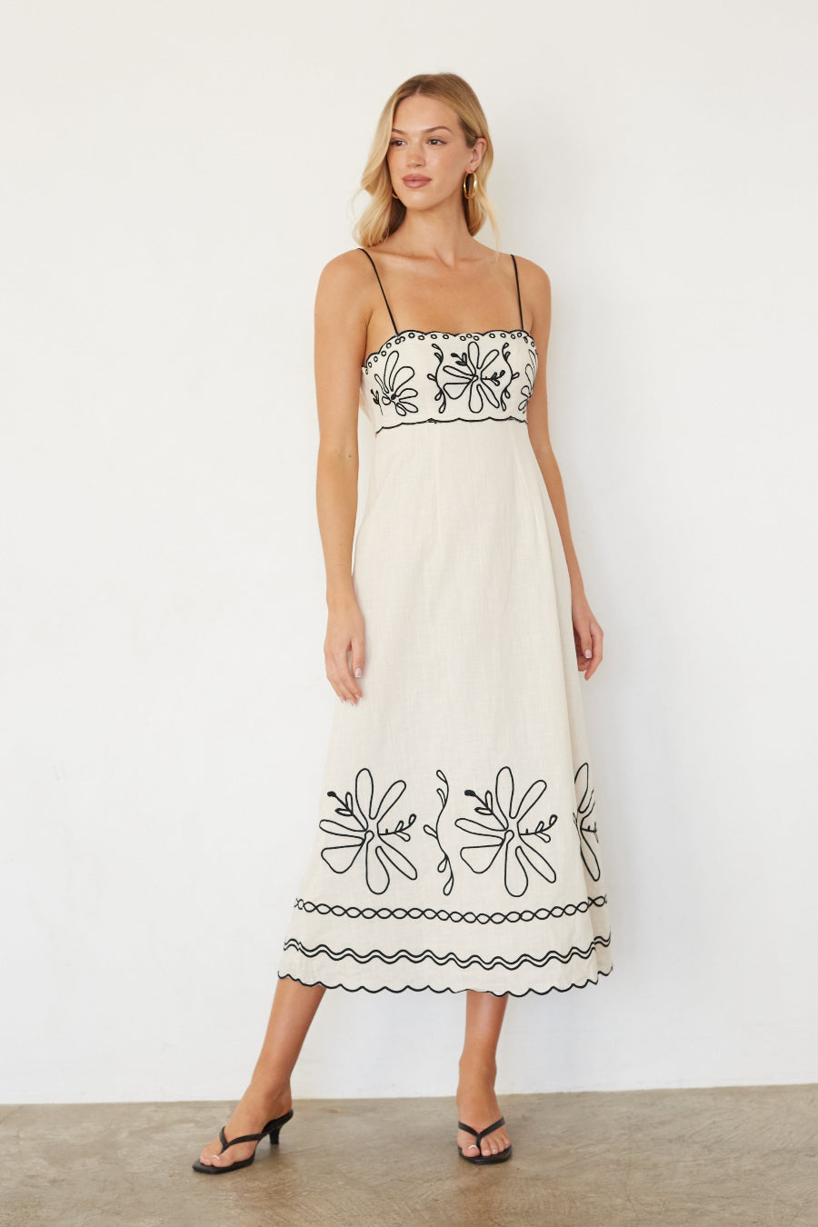 Woman wearing a white dress with black floral embroidery against a white background
