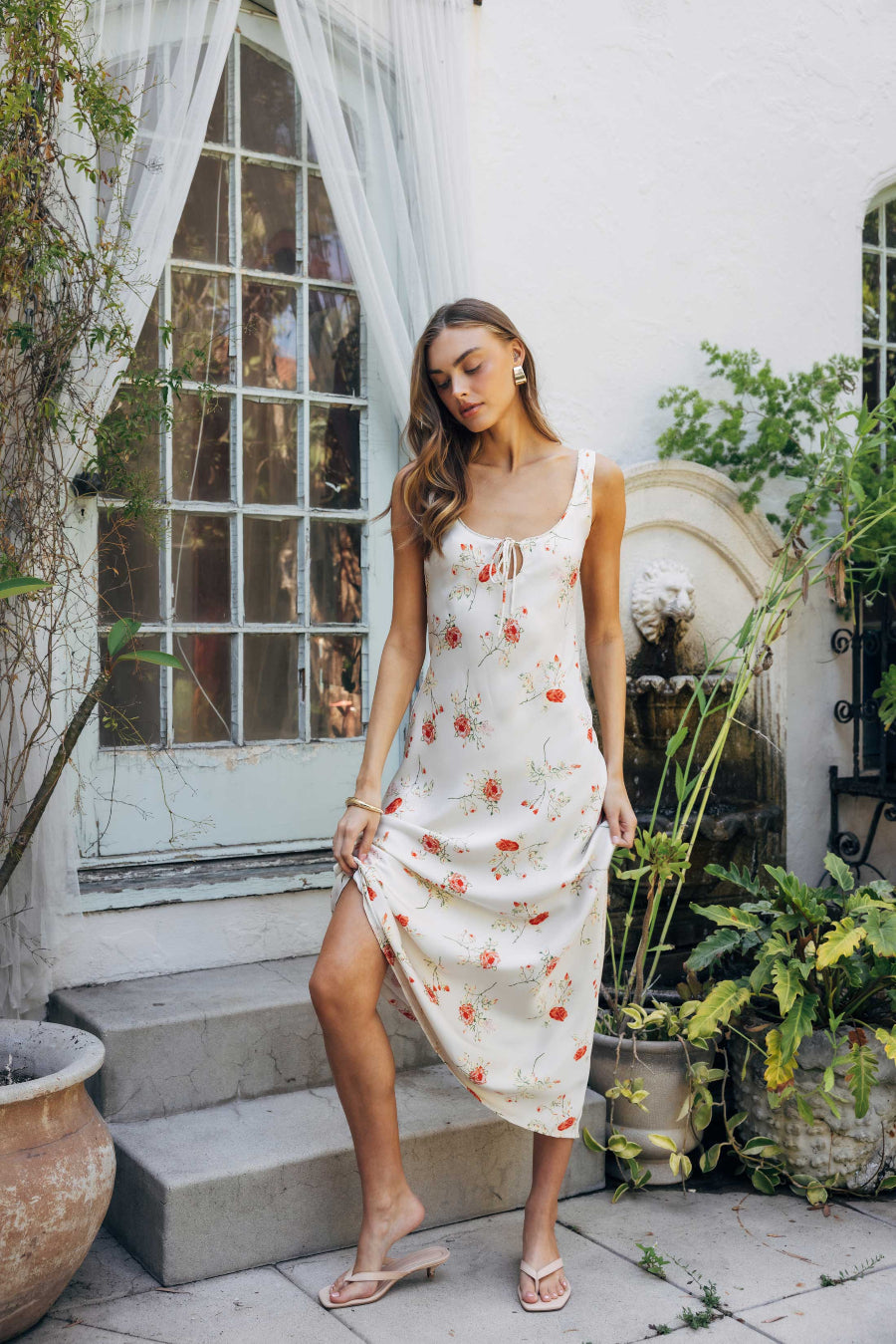 Woman in a floral dress standing outdoors near a white building with large windows.