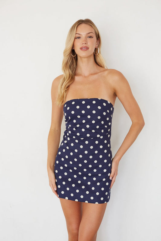 Woman wearing a navy strapless dress with white polka dots on a plain background