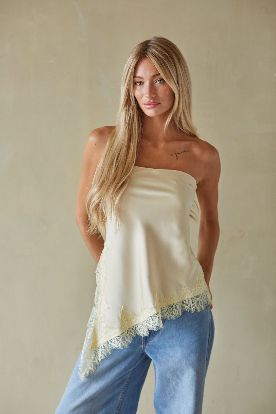 Woman wearing a strapless top with lace trim and blue jeans against a beige background