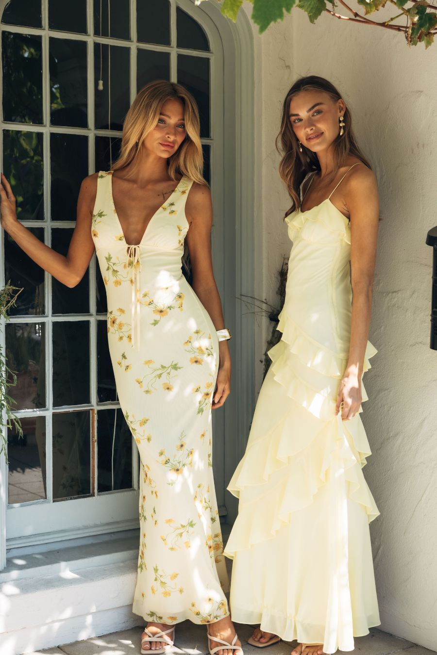 Two women in elegant dresses standing outdoors near a door.