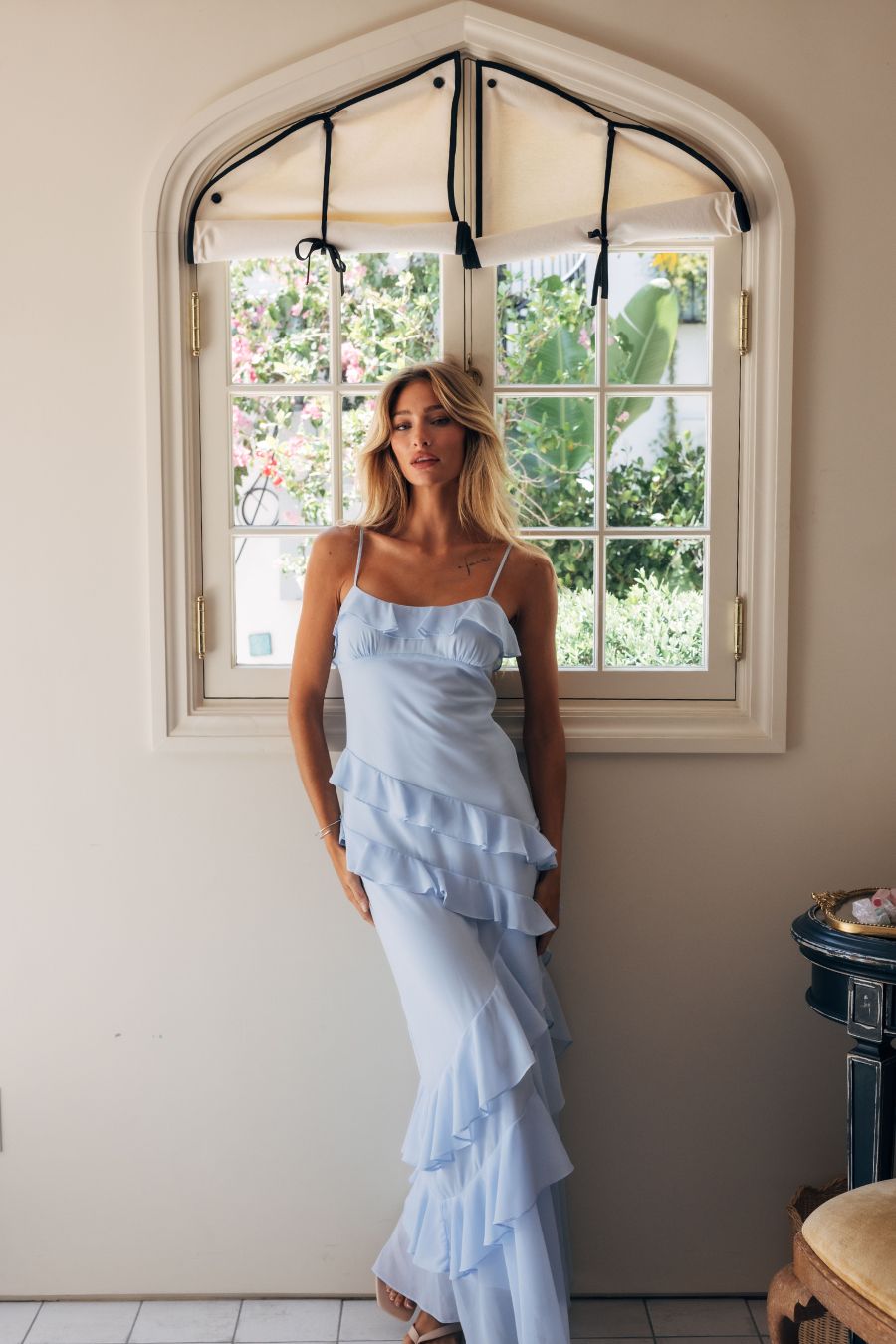 blue-image | Woman in a light blue dress standing in a room with a large window.